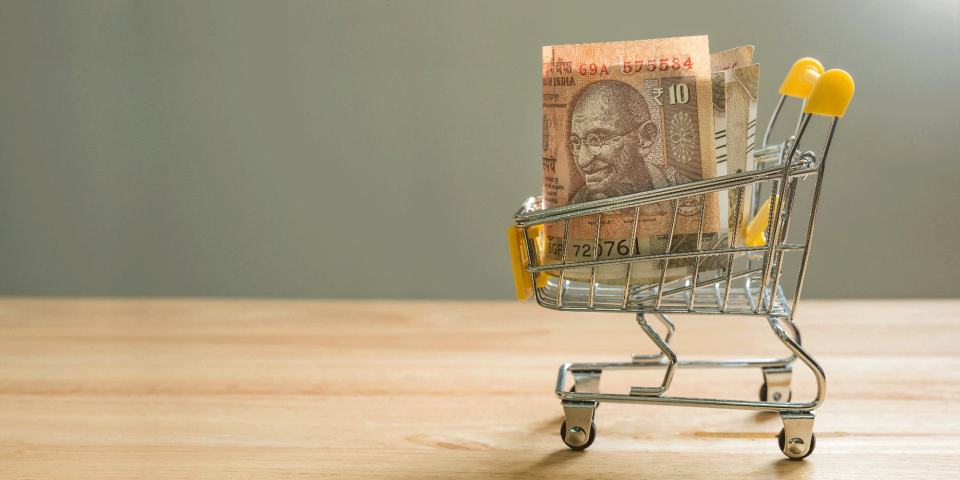 Indian rupee bills in mini shopping cart on a wooden desktop